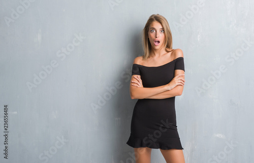 Beautiful young woman standing over grunge grey wall wearing elegant dress afraid and shocked with surprise expression, fear and excited face.