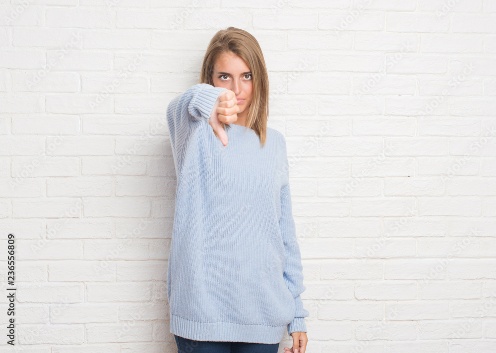 Beautiful young woman over white brick wall looking unhappy and angry showing rejection and negative with thumbs down gesture. Bad expression. Beautiful young woman over white brick wall looking unhappy and angry showing rejection and negative with thumbs down gesture. Bad expression.