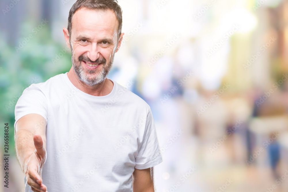 Middle age hoary senior man wearing white t-shirt over isolated background smiling friendly offering handshake as greeting and welcoming. Successful business. Middle age hoary senior man wearing white t-shirt over isolated background smiling friendly offering handshake as greeting and welcoming. Successful business.