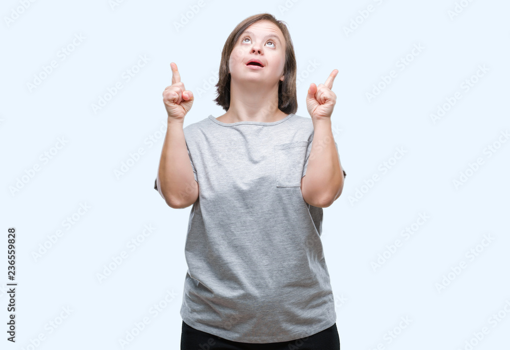 Young adult woman with down syndrome over isolated background amazed and surprised looking up and pointing with fingers and raised arms. Young adult woman with down syndrome over isolated background amazed and surprised looking up and pointing with fingers and raised arms.