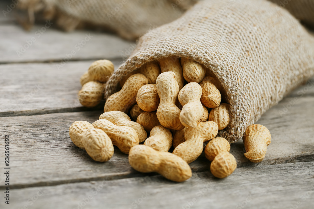 Peanuts in a miniature burlap bag on old, gray wooden surface Peanuts in a miniature burlap bag on old, gray wooden surface