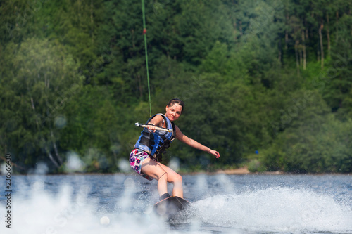 Fototapeta Naklejka Na Ścianę i Meble -  Young pretty slim brunette woman riding wakeboard on wave of motorboat in summer lake