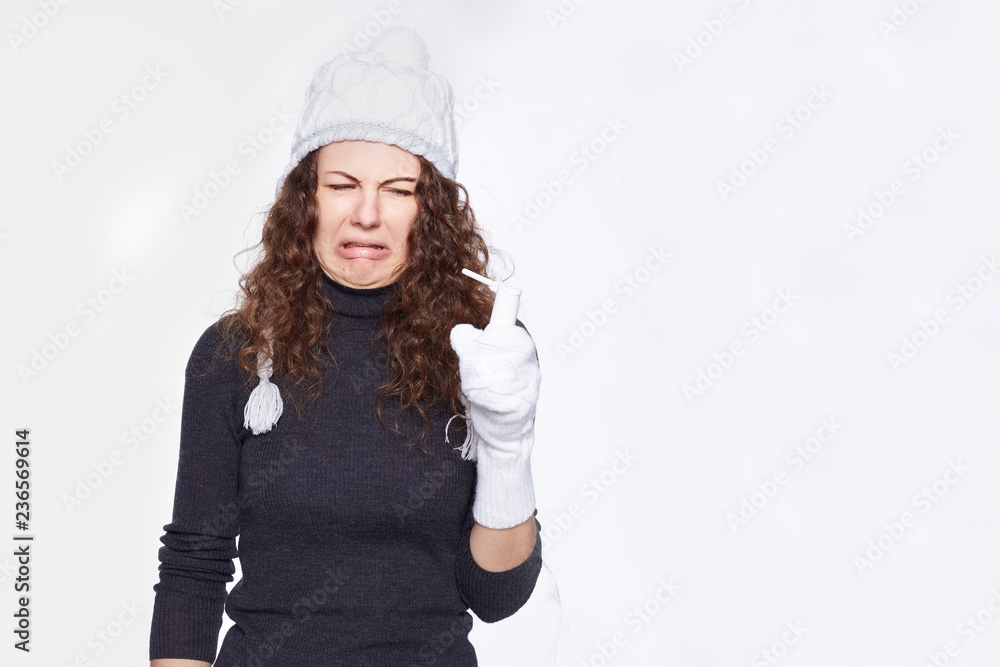 Disgusted funny female feels aversion towards treatment, frowns face, gestures, has squeamish expression, isolated over white wall. Emotional lady spray medicine in throat as feeling pain and sick. Disgusted funny female feels aversion towards treatment, frowns face, gestures, has squeamish expression, isolated over white wall. Emotional lady spray medicine in throat as feeling pain and sick.