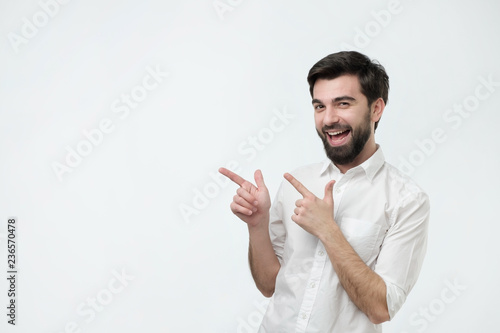 Happy beautiful bearded hispanic man looking at camera, smiling and pointing aside with hand.