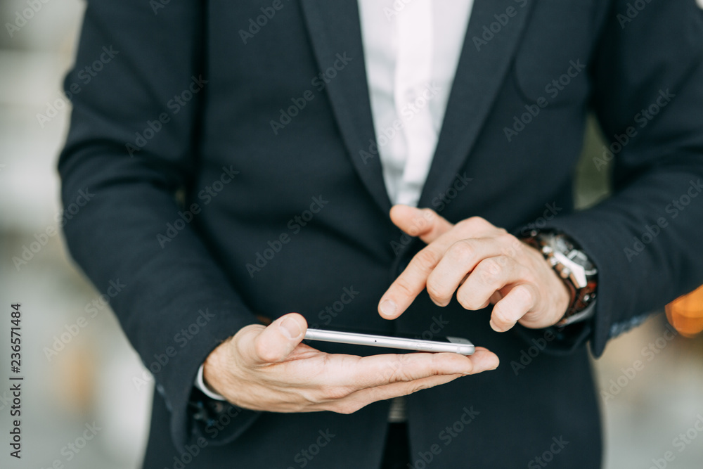 The phone on the hand of a business man, with his hand and finger touches. Blank for designers with bokeh. The phone on the hand of a business man, with his hand and finger touches. Blank for designers with bokeh.
