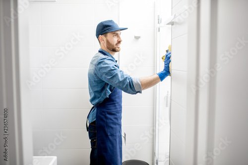 Man as professional cleaner wiping the shower door with cotton wiper in the white bathroom