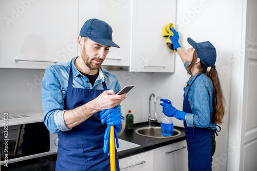 Man and woman as a professional cleaners in uniiform having fun during the work on the kitchen