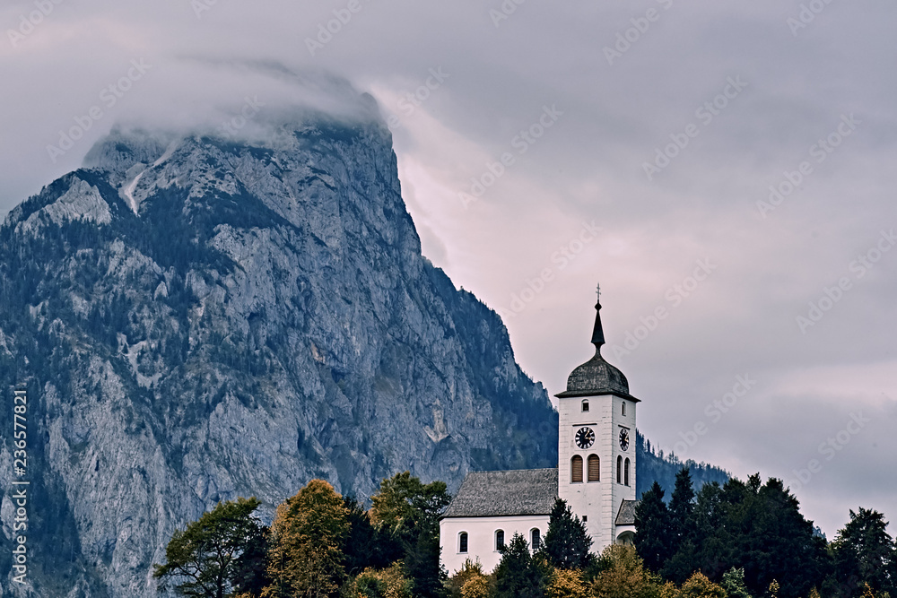 Beautiful scenic sunset over Austrian alps lake. Church on the rock with clouds over Traunstein mountain at the alps lake near Hallstatt Salzkammergut Austria