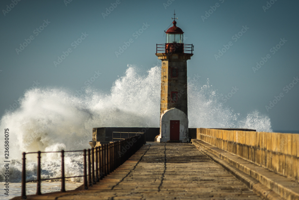 lighthouse with a big wave of water from the ocean with blu sky