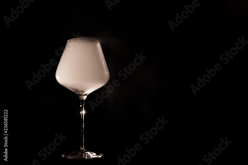 Burgundy crystal transparent red wine glass fully filled with white thick smoke, isolated close up on black background in the studio. Chemical party concept