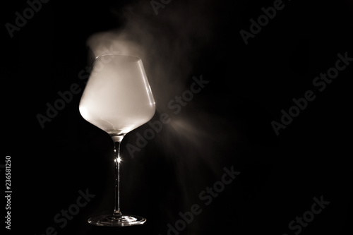 Burgundy crystal transparent red wine glass fully filled with white thick smoke, isolated close up on black background in the studio. Wine tasting concept
