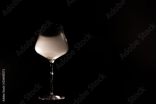 Burgundy crystal transparent red wine glass half filled with white thick smoke, isolated close up on a black background in studio. Wine tasting concept