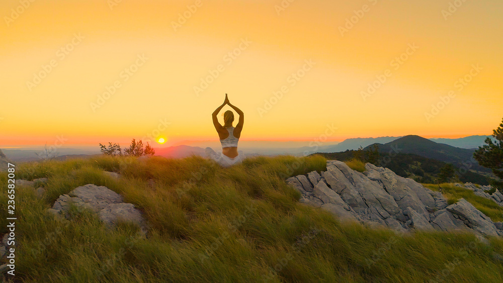 Fit young woman holding a yoga pose while sitting and watching the golden sunset