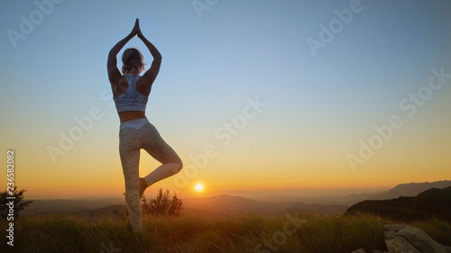 Fototapeta Naklejka Na Ścianę i Meble -  AERIAL: Flexible Caucasian woman holds a scorpion pose in front of the sunrise.