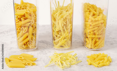 Different types of raw pasta in containers on a light background. Fettuccine, fusilli, penne. Storage products at home