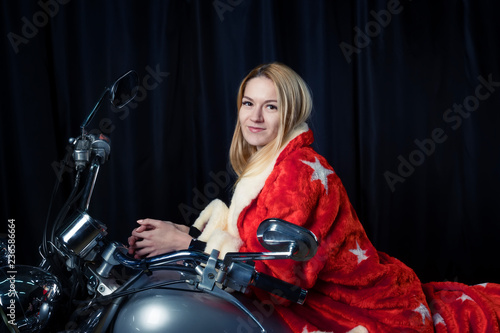 Beautiful blonde in Santa Claus outfit on a motorcycle carries gifts