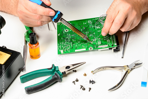 The electronics technician replaces the non-working element of the electronic device with a soldering iron. The hands of an electronics engineer, repair electronic devices concept.