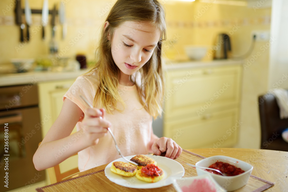 Cute little girl enjoying her breakfast at home. Pretty child eating pancakes with strawberry sauce before school.