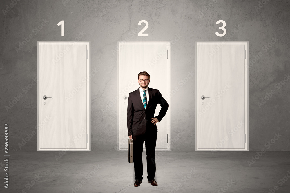 Fototapeta premium Businessman in grey room with three numbered white door behind his back 