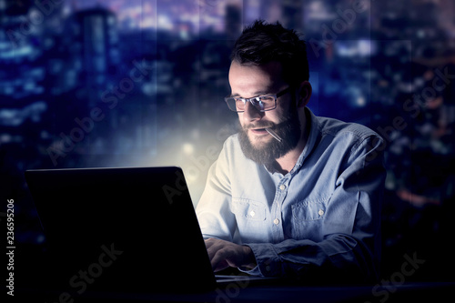 Young handsome businessman working late at night in the office with blue lights in the background © ra2 studio