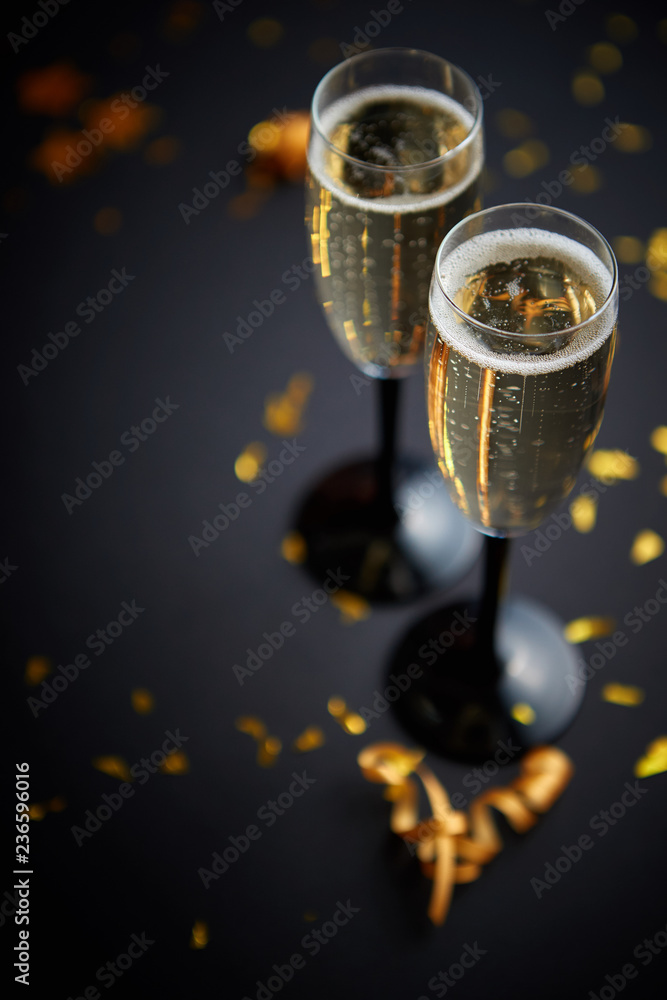 Two glasses full of sparkling champagne wine with golden decoration of confetti and serpentines on black elegant background. Top view with copy space. Festive or party concept. Two glasses full of sparkling champagne wine with golden decoration of confetti and serpentines on black elegant background. Top view with copy space. Festive or party concept.