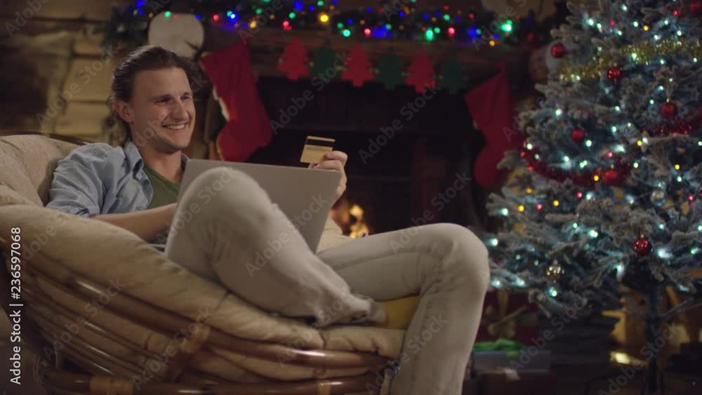 Handsome young man shopping online while talking in video chat by using laptop and credit card in Xmas night Handsome young man shopping online while talking in video chat by using laptop and credit card in Xmas night