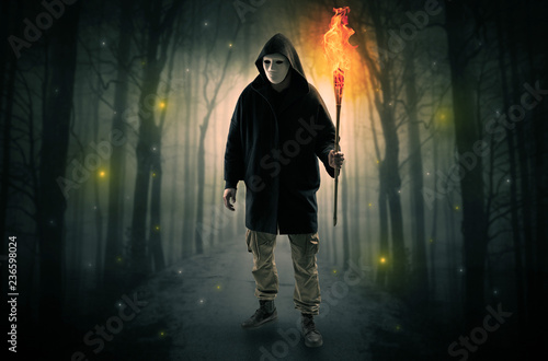 Mysterious man coming from a path in the forest with burning flambeau concept 