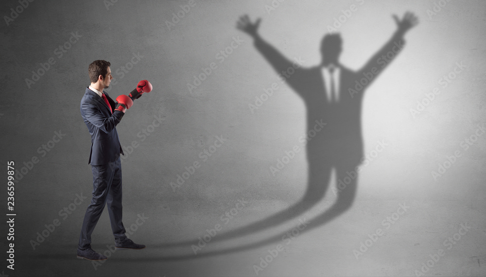 Fototapeta premium Businessman with boxing gloves fighting with disarmed businessman shadow 
