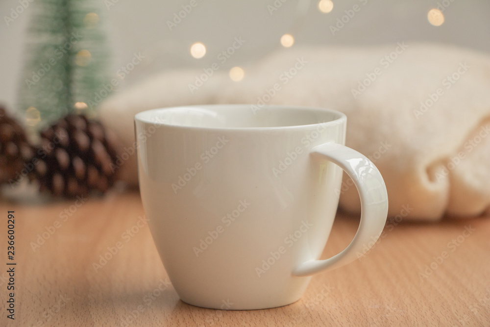 white cup of hot chocolate on table with blur christmas light,pine cones,mini tree and sweater. white cup of hot chocolate on table with blur christmas light,pine cones,mini tree and sweater.