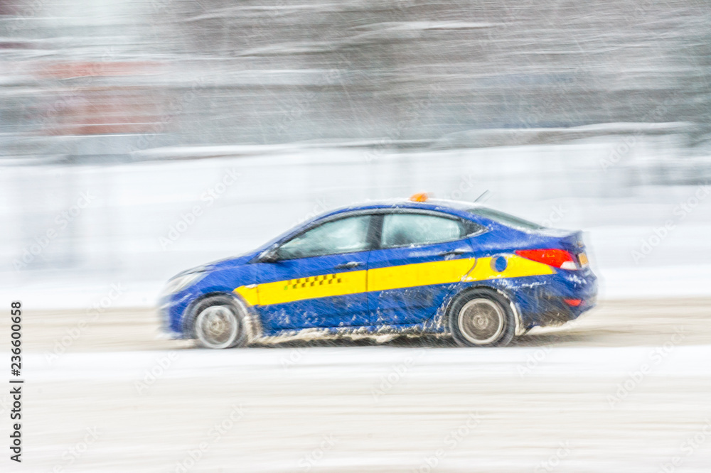 Driving in snow. Motion in blur blue cab in heavy snowfall in city road. Abstract blur winter weather background.
