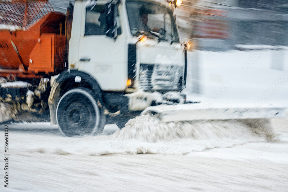 Snow plow truck removes snow from the city road. Snowstorm in the city - seasonal abstract motion blur background