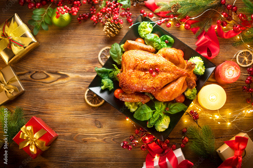 Christmas family dinner. Roasted chicken on holiday table, decorated with gift boxes, burning candles and garlands. Roasted turkey over wooden background. Top view, flatlay