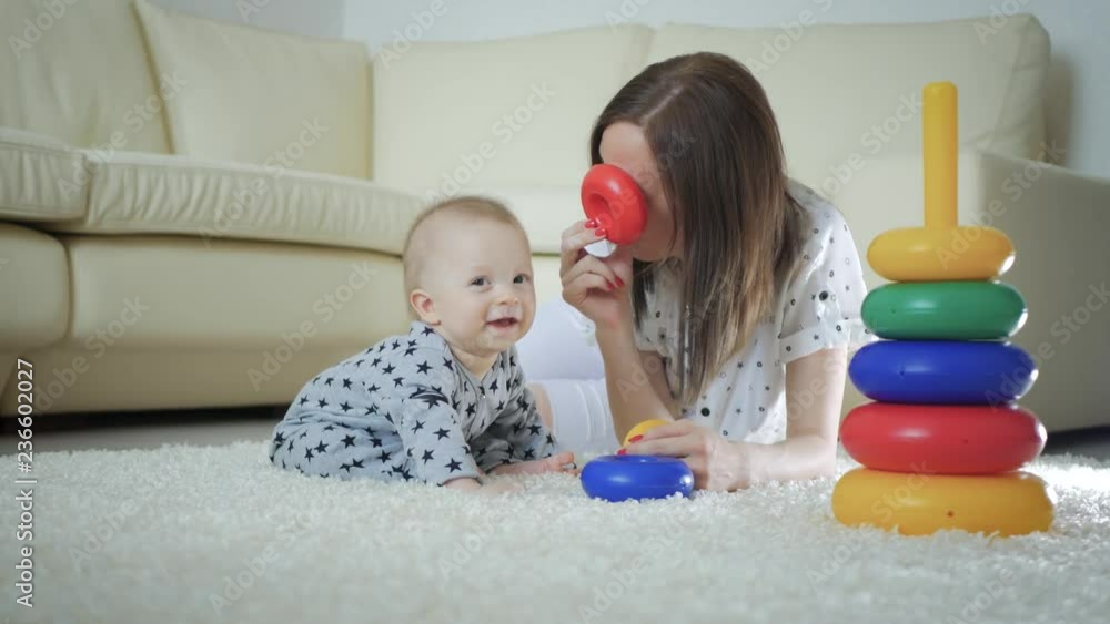Joyful mother and baby playing with toys on a carpet at home. Side view of a happy mother and son playing with toys on the floor. Happy family spend fun time together. Joyful mother and baby playing with toys on a carpet at home. Side view of a happy mother and son playing with toys on the floor. Happy family spend fun time together.