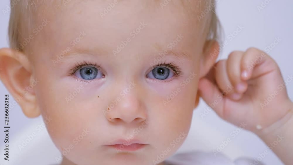 Innocent blue eyes baby portrait playing with ear, itchiness, scratch Innocent blue eyes baby portrait playing with ear, itchiness, scratch