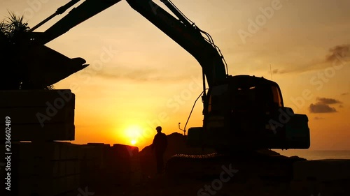 Wallpaper Mural Construction Video At construction site close up The silhouette excavator is digging ground and lifting a large mortar, with engineering and construction workers to help with colorful sunset . Torontodigital.ca