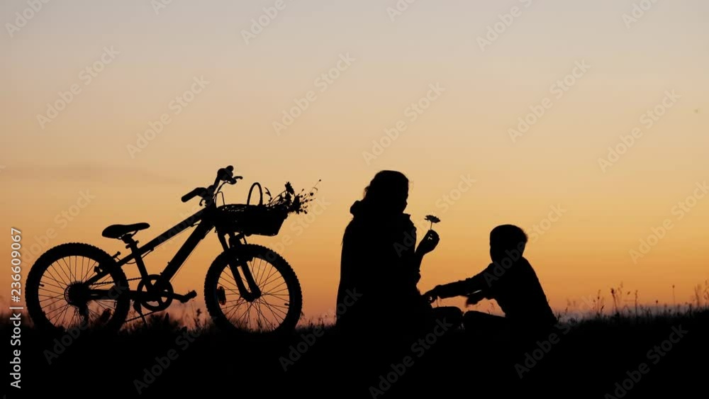Mother and children silhouette near bike on hill, sunset sky Mother and children silhouette near bike on hill, sunset sky