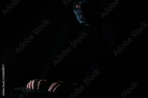 A man in a mask prints on the keyboard in the dark © alexkich
