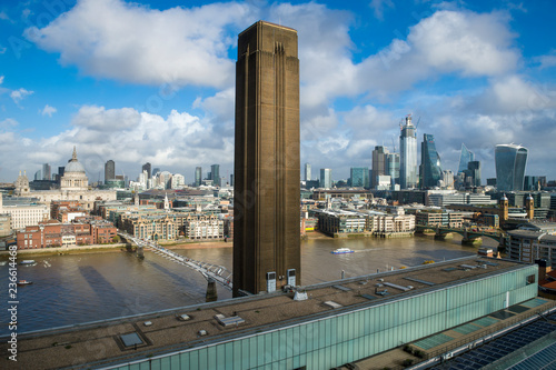 Brown brick tower of a former power station standing on the South Bank of the River Thames above the skyline of the City of London financial district