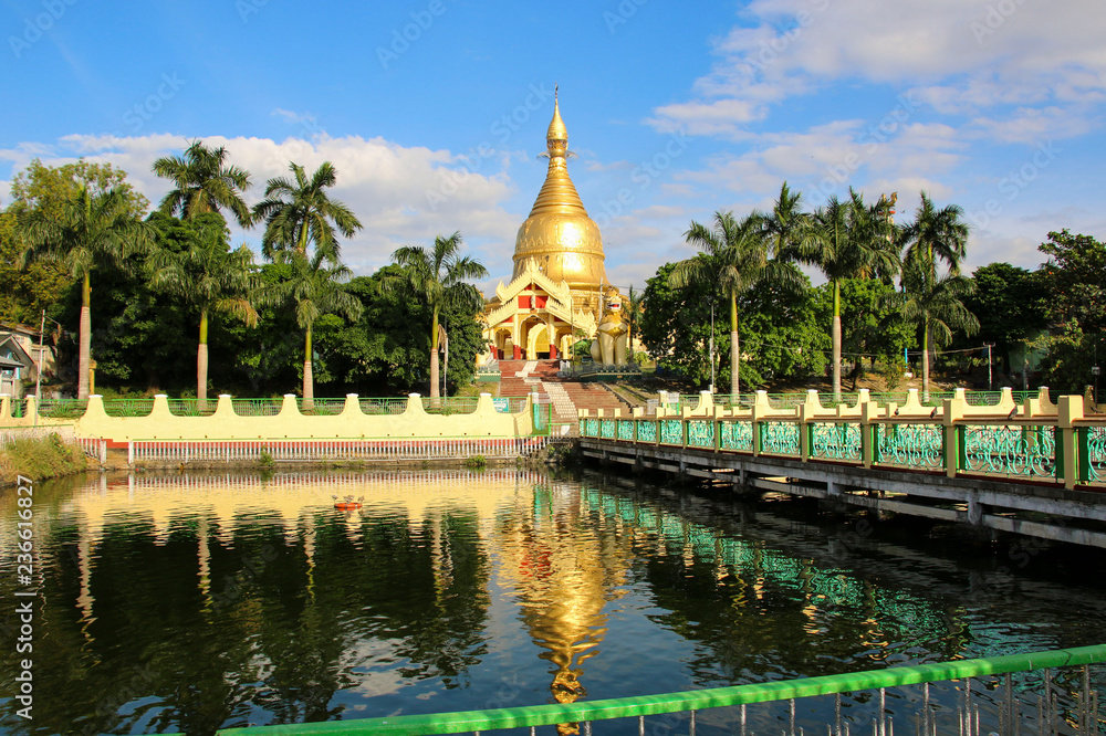 One of the many golden stupas against the blue sky and pond with reflection in the water in Yangon, Myanmar (Burma)