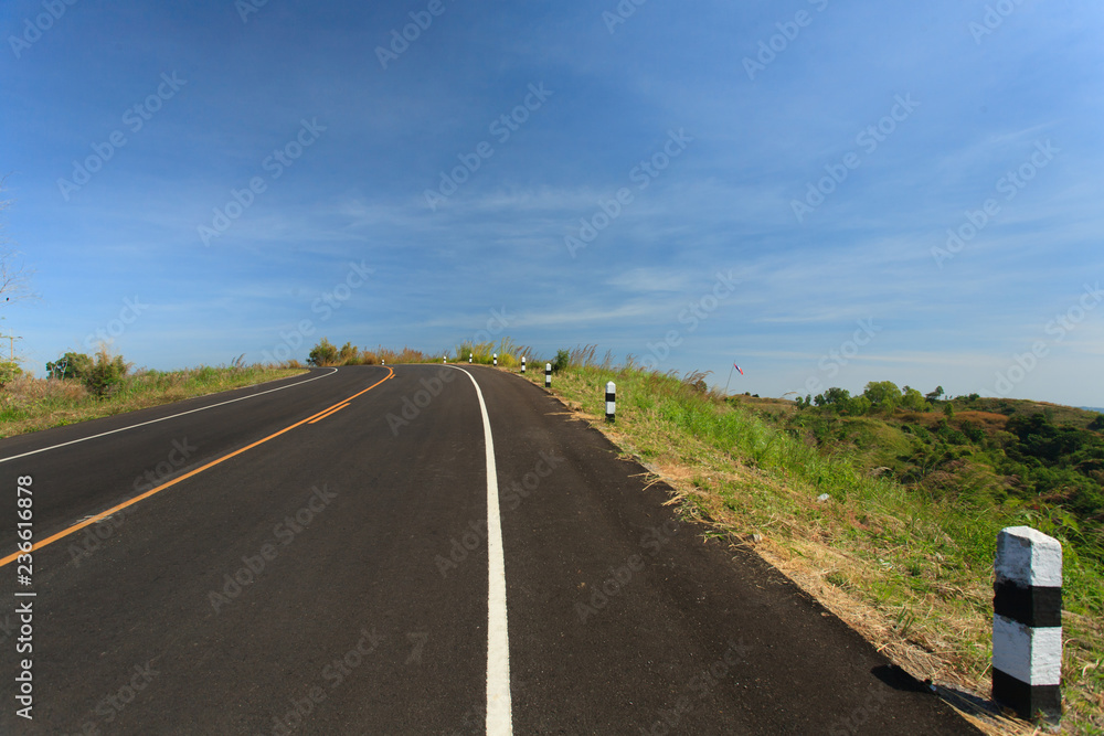 Road with grass flower , clearly blue sky  in countryside of Thailand.