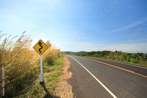 Traffic signs erected at the side of road with grass flower , clearly blue sky in countryside of Thailand.