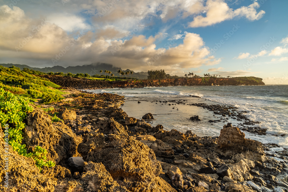 Waves Breaking into Makawehi Bluff while warm sunrise light illuminates the clouds, Kauai, Hawaii
