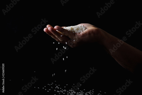 Rice falling through the fingers of male hand. Dark background