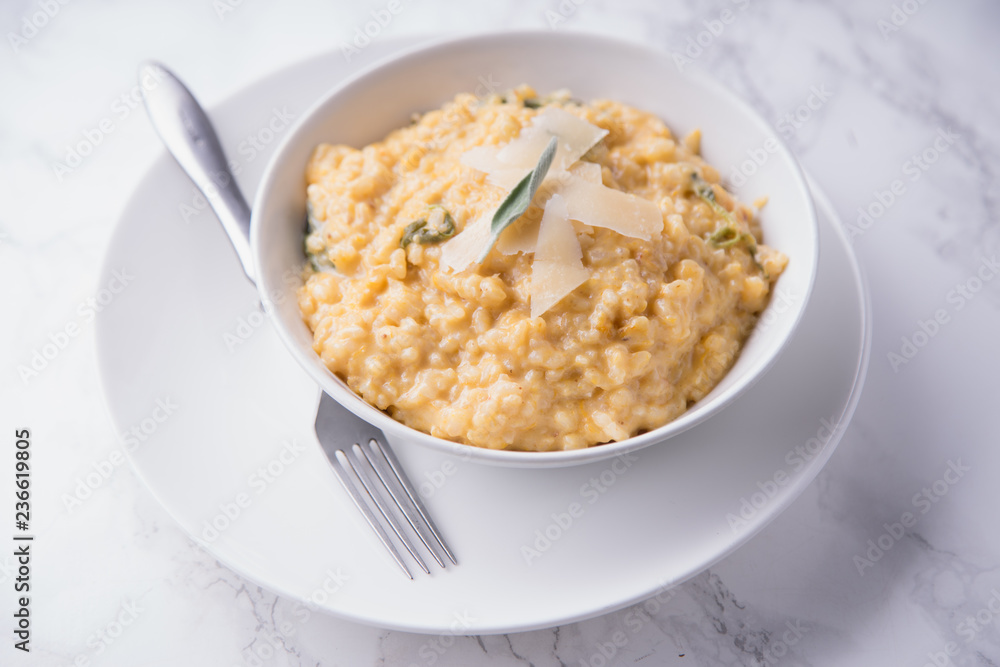 Pumpkin risotto with parmesan and sage. White marble background