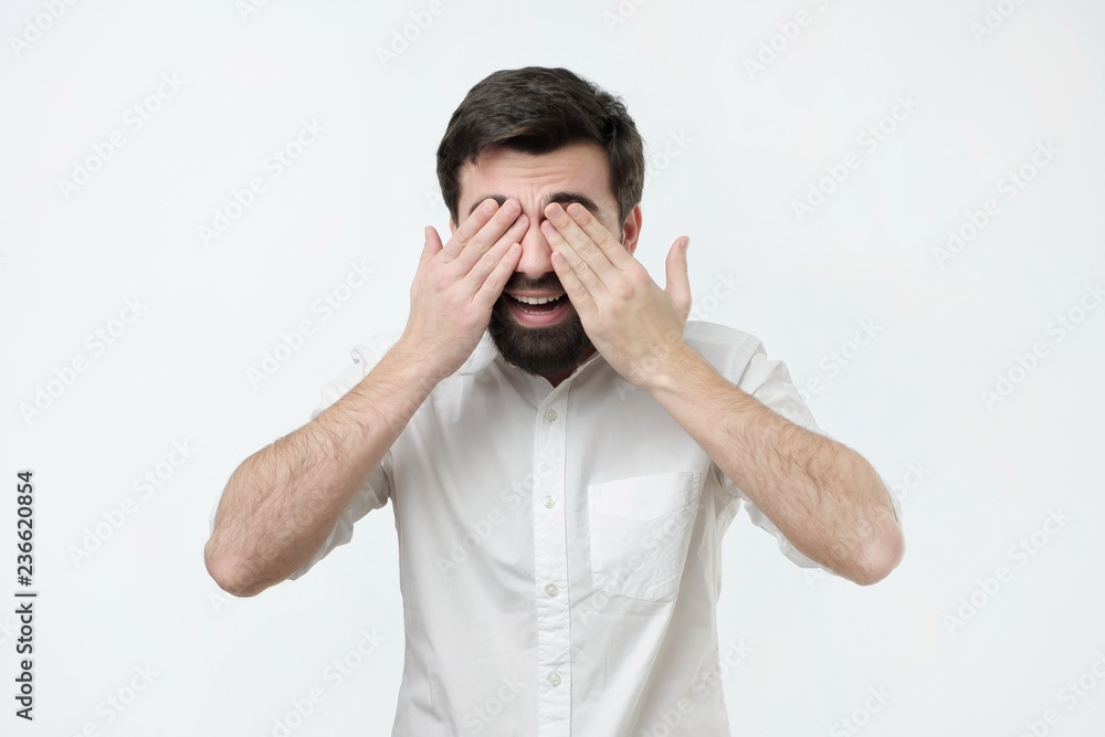 Time to receive surprise. Hispanic man in white shirt covering eyes with palms and smiling, being curious to see a gift Time to receive surprise. Hispanic man in white shirt covering eyes with palms and smiling, being curious to see a gift