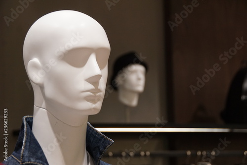 White male mannequin's head with another male mannequin's head in black hat in the background