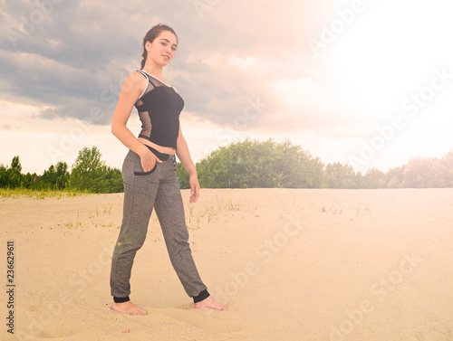 Sporty young brunette girl standing on the sand in the desert sunset over the forest.