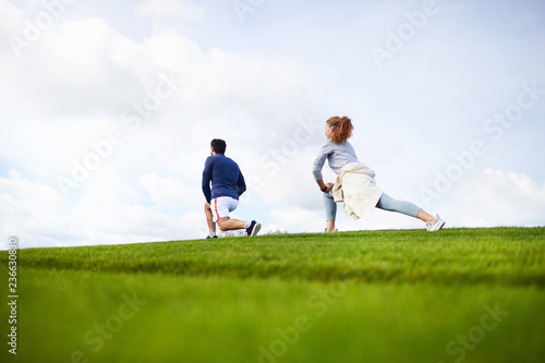Young sporty couple doing exercise for leg stretching while training on green grass
