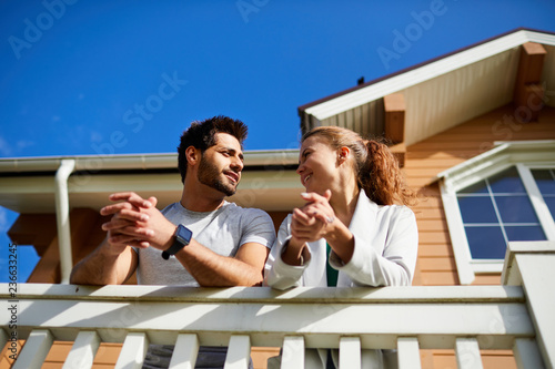 Young amorous couple standing on balcony of their new house and having talk