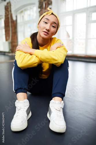 Serene young girl in activewear sitting on the floor of modern dance studio in front of camera photo